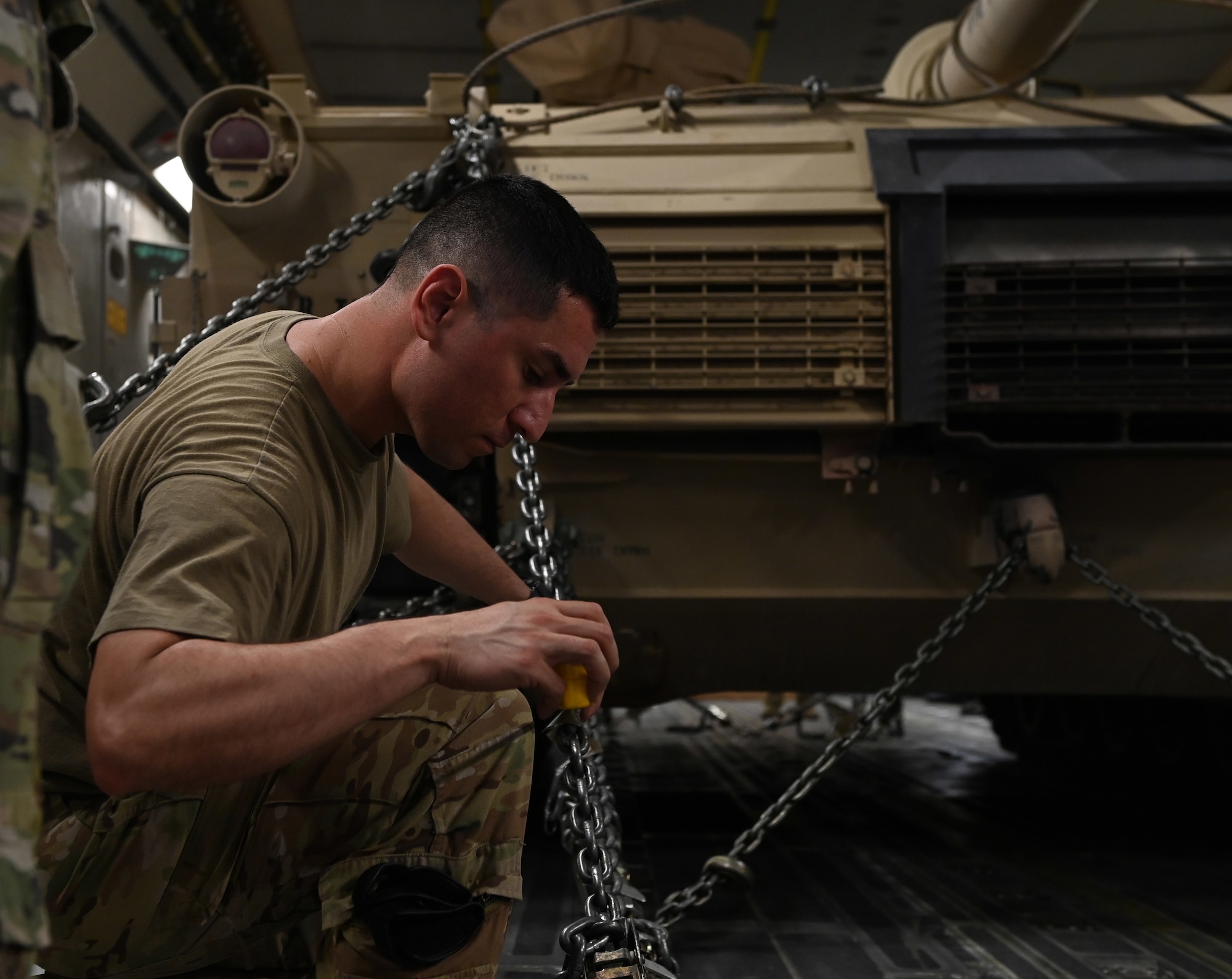U.S. Air Force Tech. Sgt. Jose Cardoza, an 816th Expeditionary Airlift Squadron loadmaster, measures the length and angle of a chain securing an M-1/A2 Abrams main battle tank Aug 27, 2022 at Ali Al Salem Air Base, Kuwait. Loadmasters thoroughly scrutinize every chain to ensure the angles and placement provide proper restraint to keep the tank secured during flight. (U.S. Air National Guard photo by Master Sgt. Michael J. Kelly)
