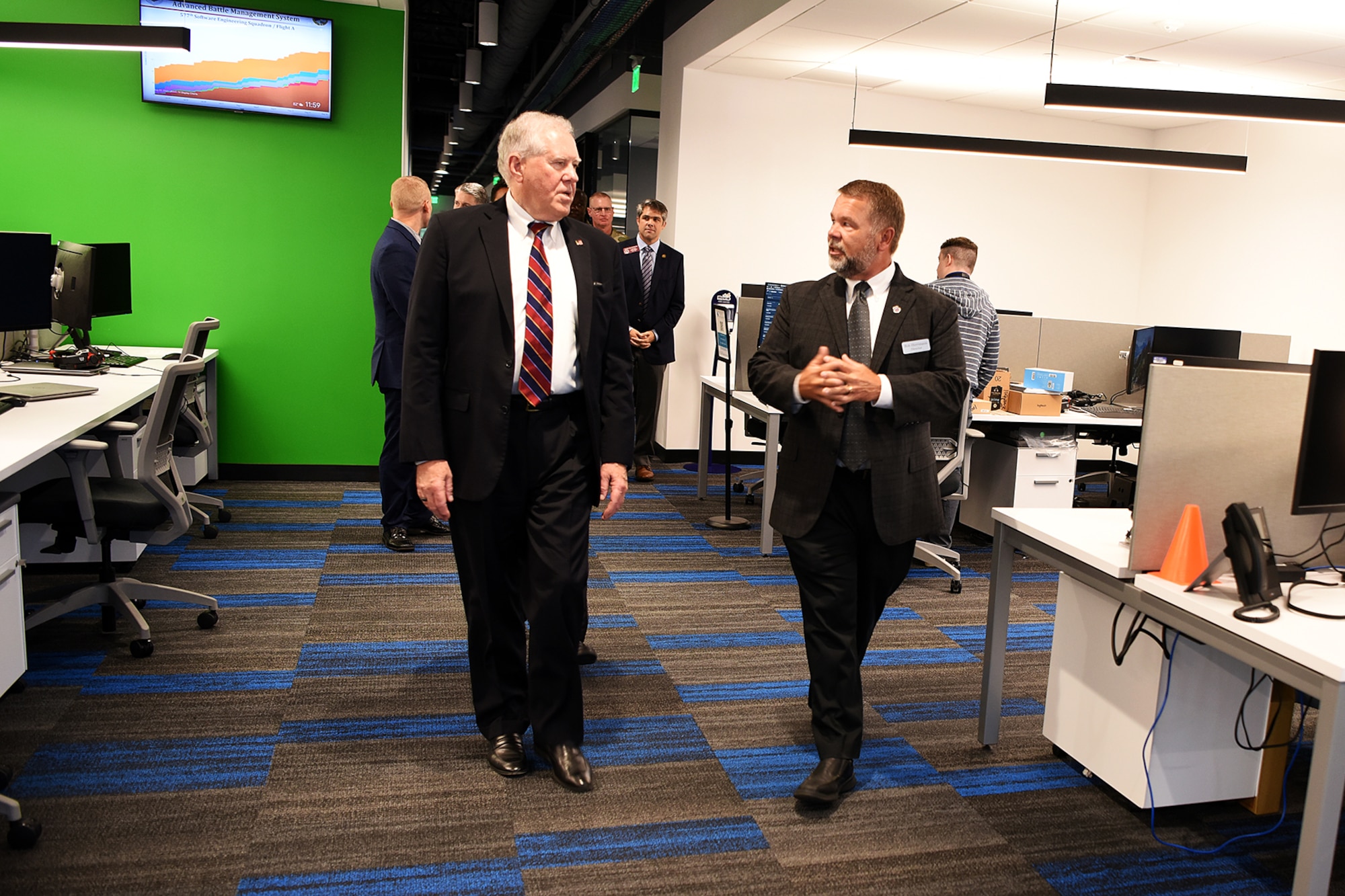 Photo shows group of people walking through a room with computers