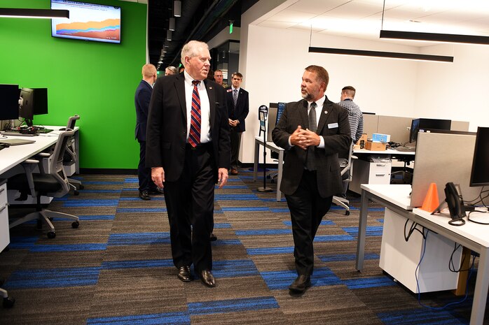 Photo shows group of people walking through a room with computers