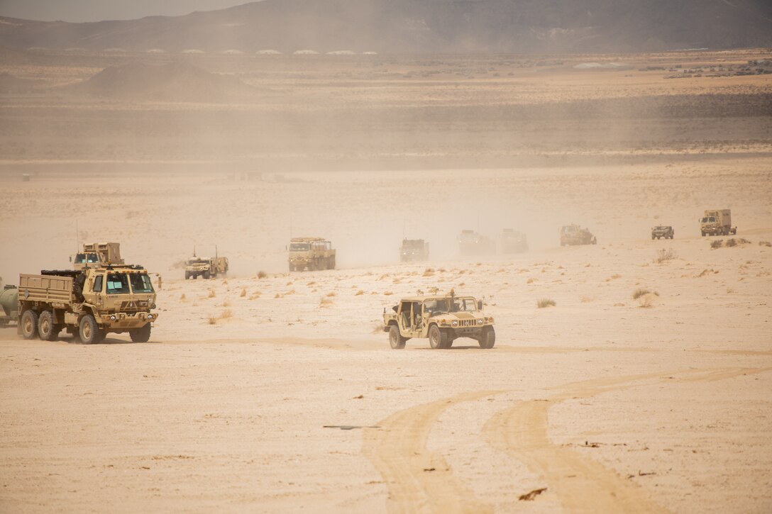 A convoy of military vehicles drive through  a desert.