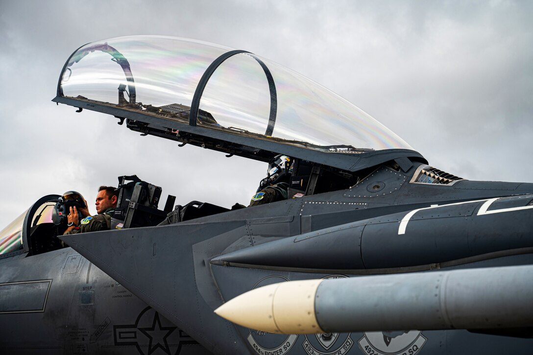 An airman sits in a plane while putting on his helmet.