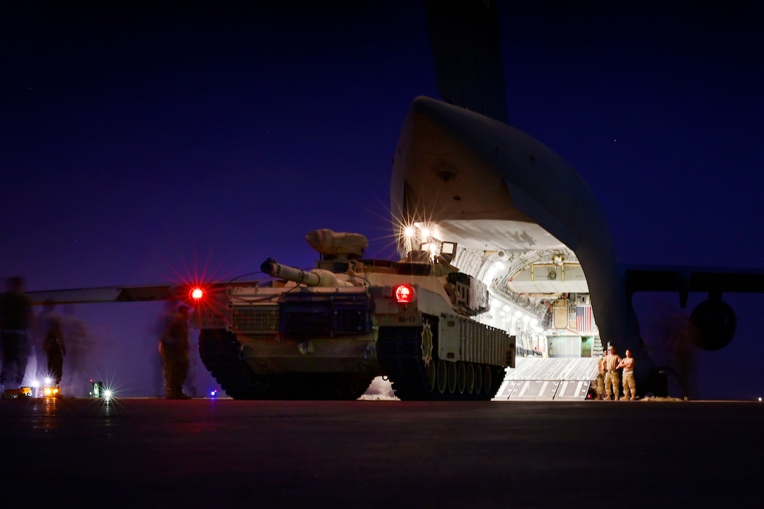 Service members watch as a tank is driven up a ramp and into the cargo hold of an aircraft