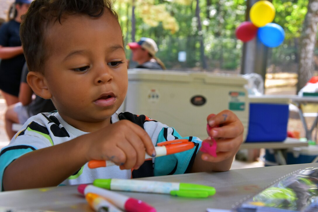 A child holds a colored marker while sitting at a picnic table outdoors.