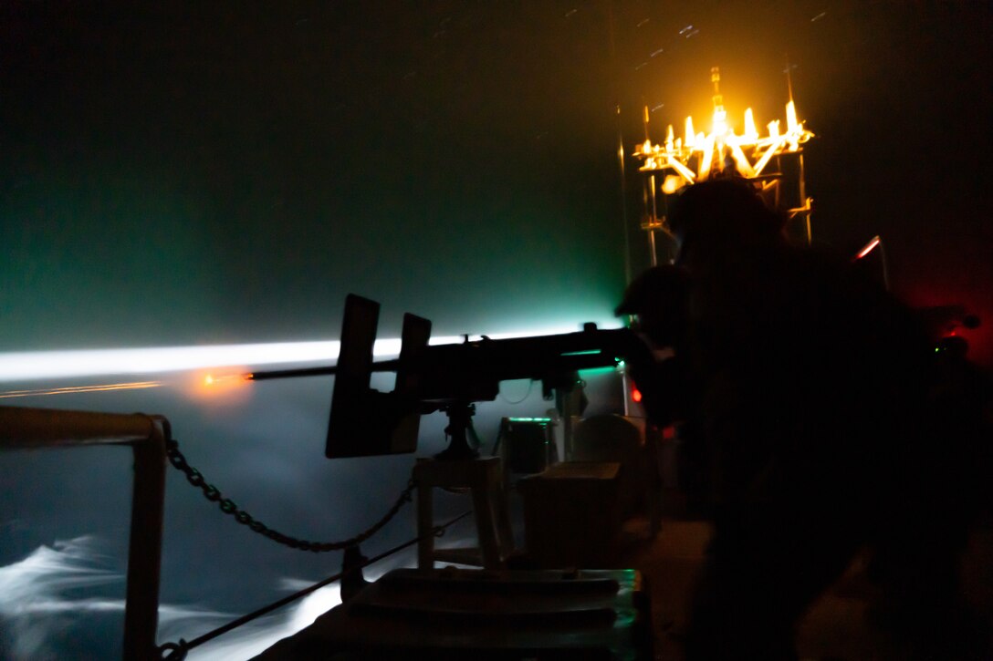 Coast Guardsmen fire weapons from a ship at night.