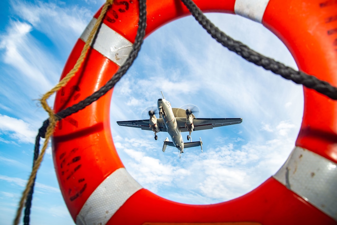 A flying aircraft is seen through the ring of a life preserver.