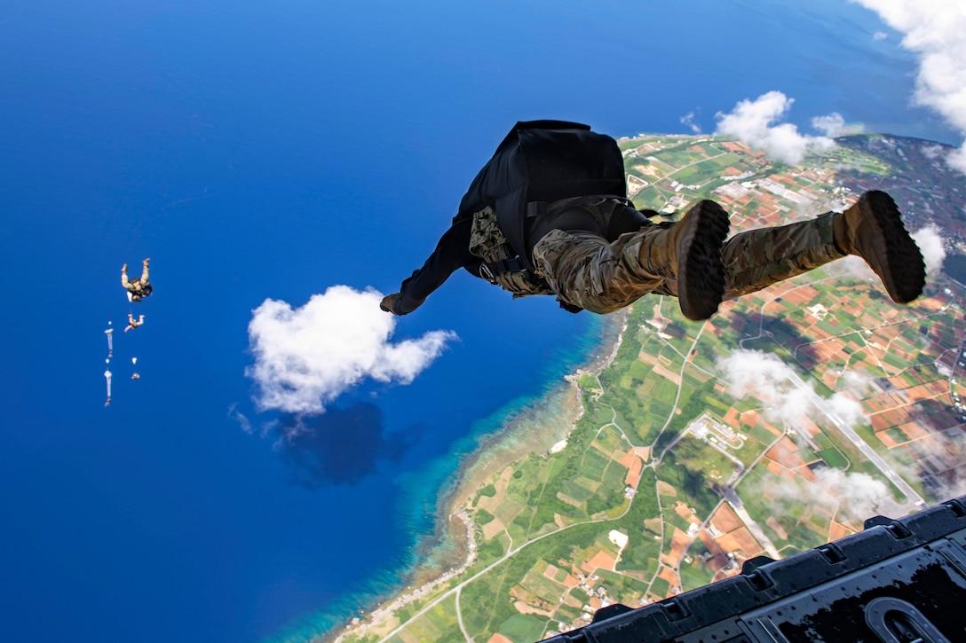 A sailor jumps of an aircraft as fellow service members free fall in the background near a cloud.