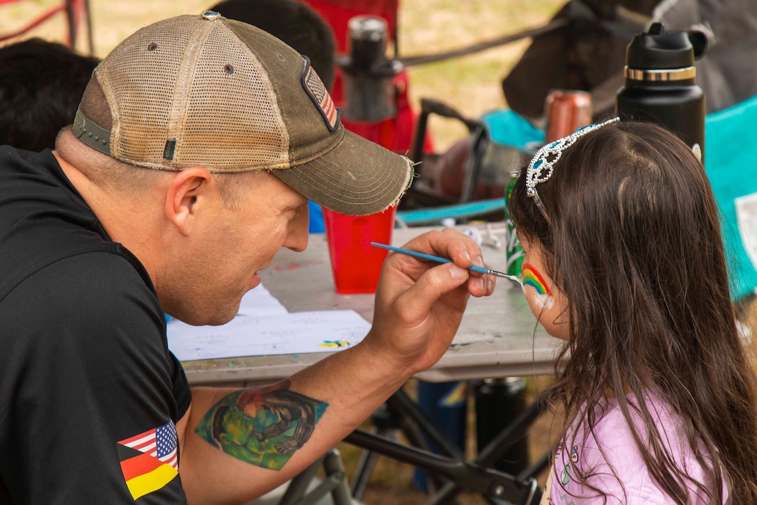 A man paints a rainbow on a child’s cheek.