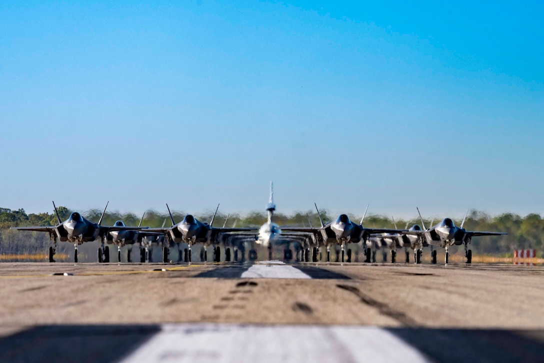 Military aircraft line up behind one another on a runway.