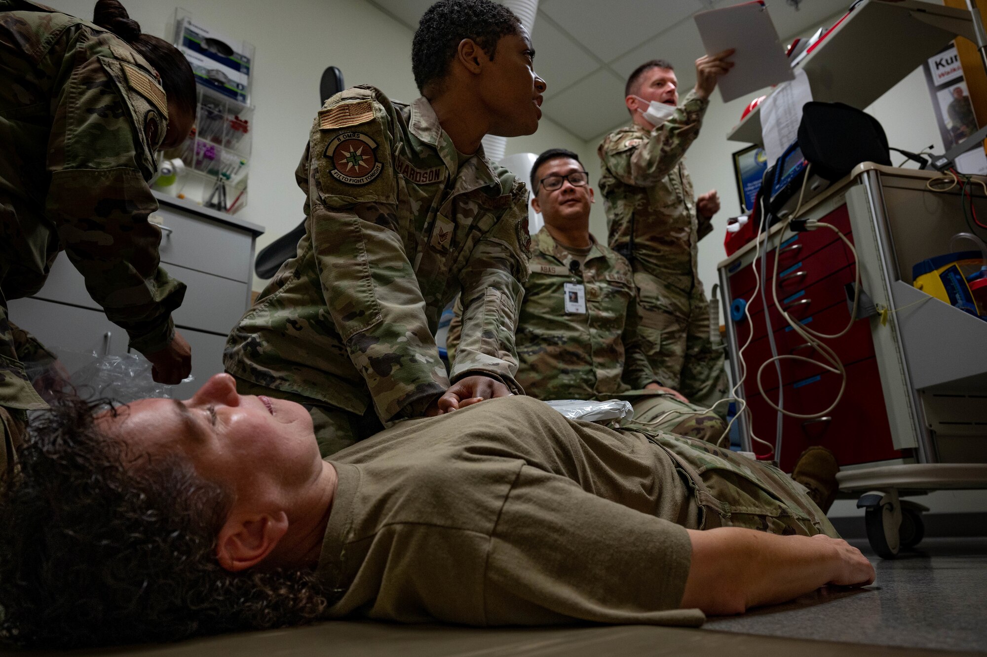 Airmen preforms chest compressions on Airman lying on the ground.