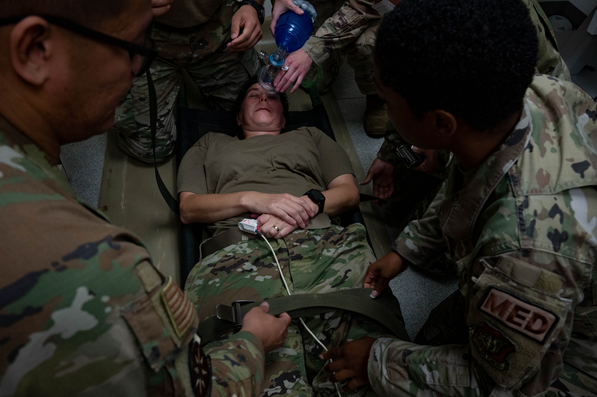 Airmen surround airmen lying on the ground and put medical mask on her face.
