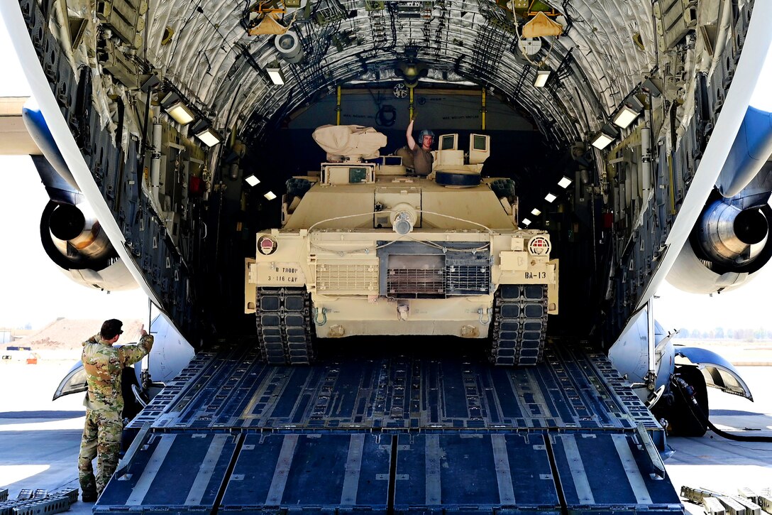 Military personnel unload a tank from the cargo hold of an aircraft.