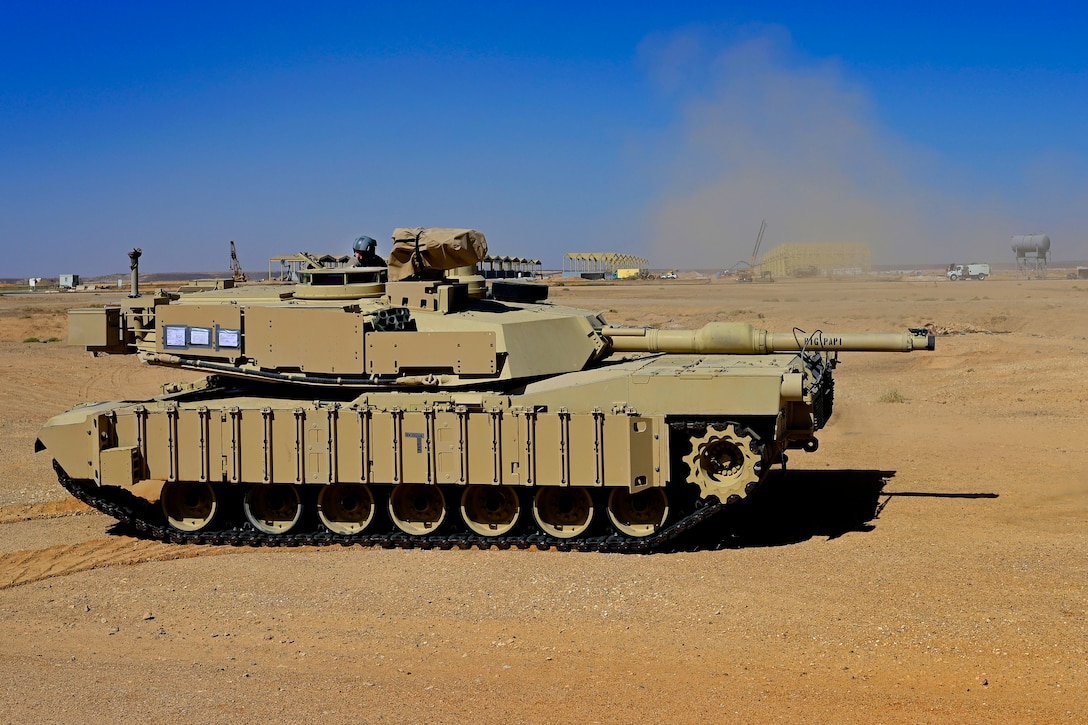 A service member drives a tank in a desert environment.