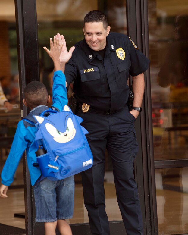 A police officer high-fives a kid outside a building.