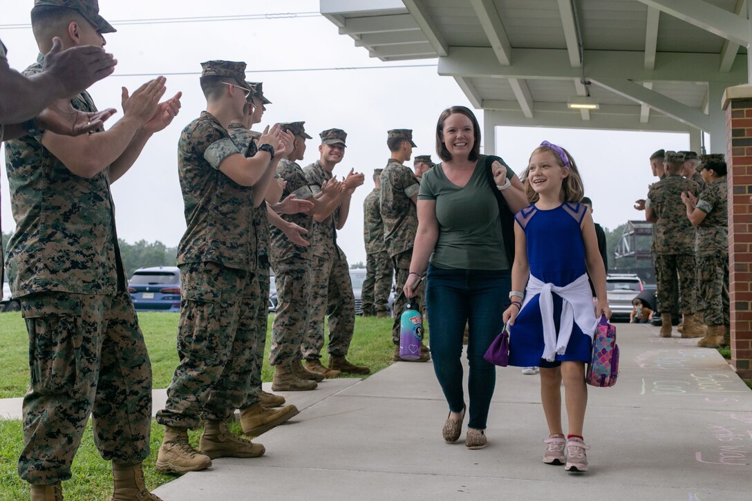 Marines stand in a line outside a school and clap for students entering.
