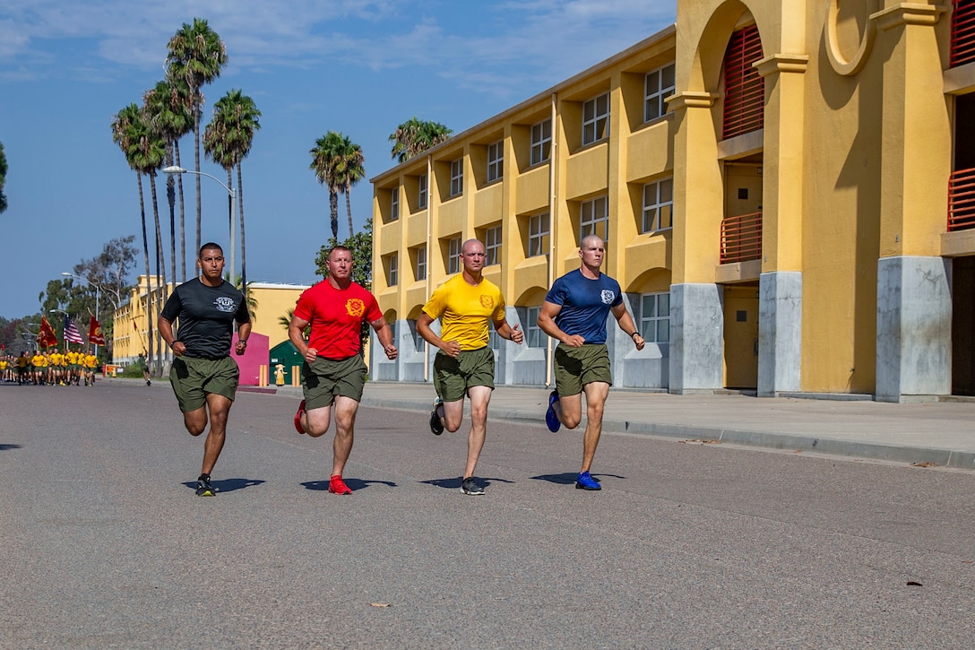 Four Marines run next to each other on a street.