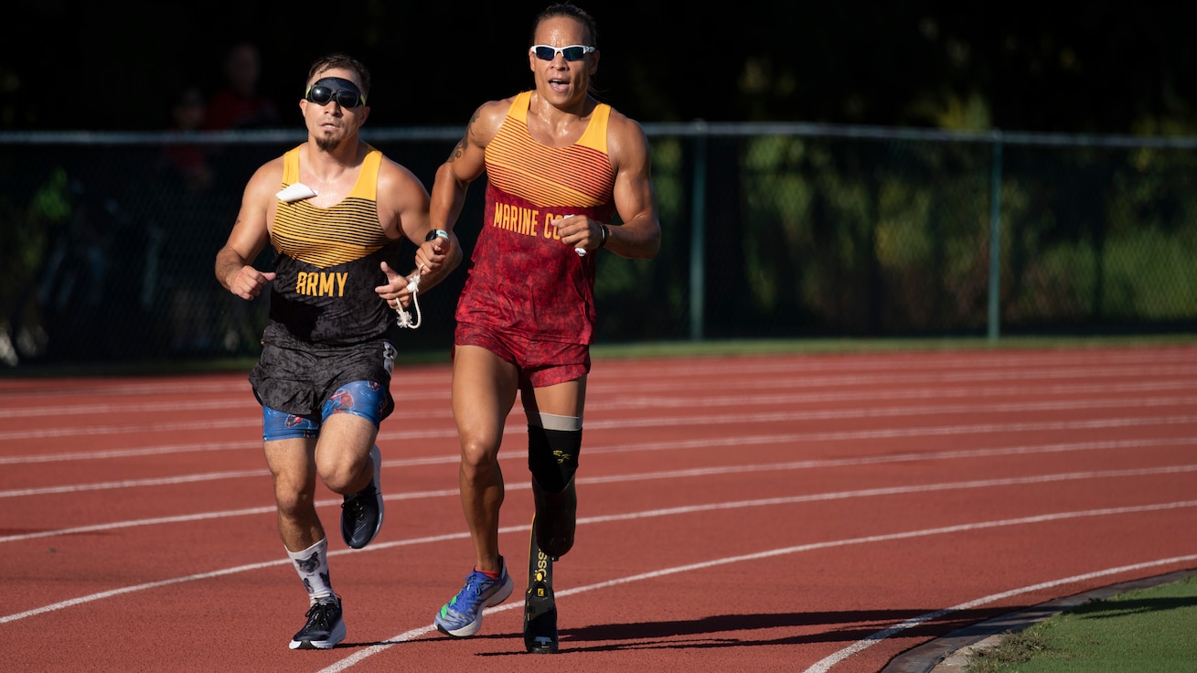 A blind Army sprinter runs with his Marine guide, who has a prosthetic left leg.