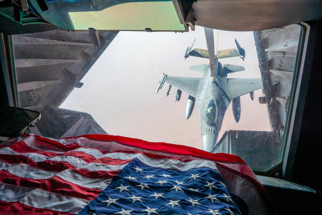 An American flag inside an aircraft as an aircraft is seen through a window receiving fuel.