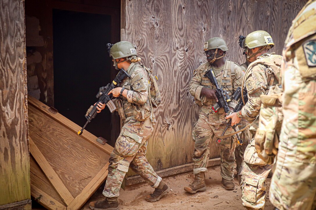 A group of soldiers stand together before entering a wooden structure.