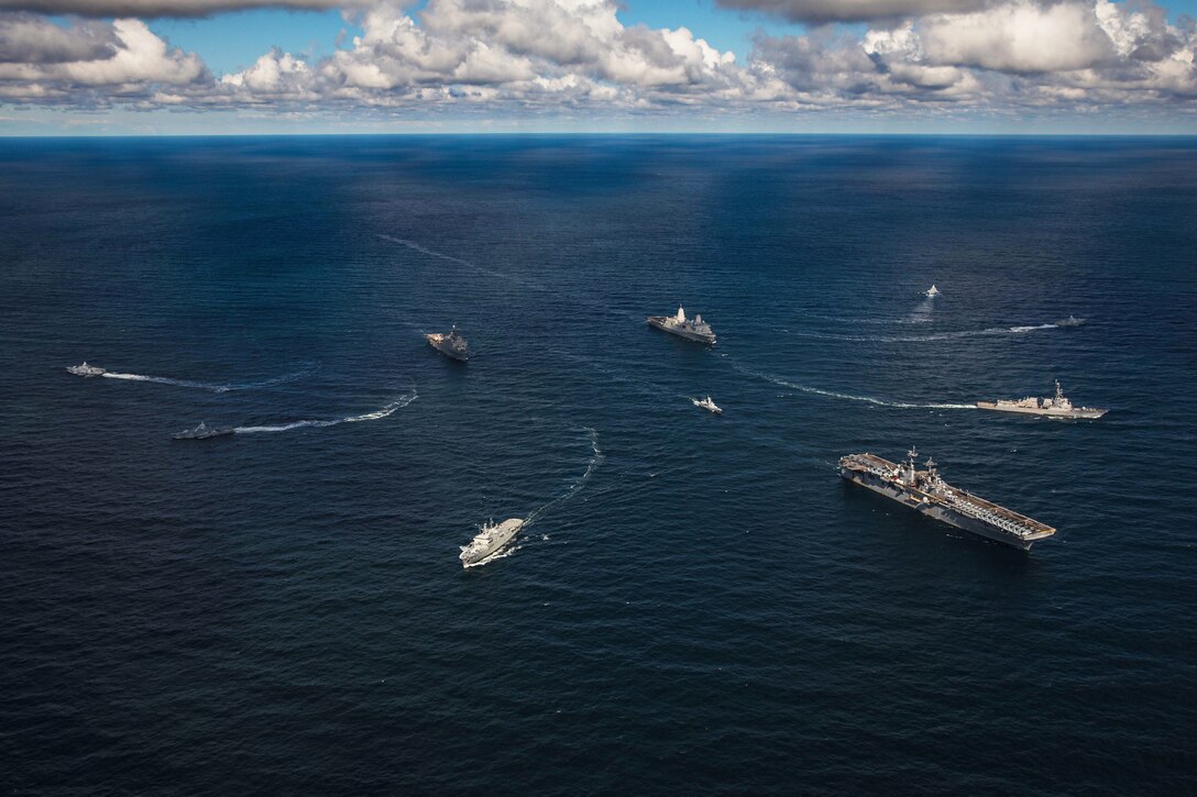A group of military ships veer away from each other in the ocean.