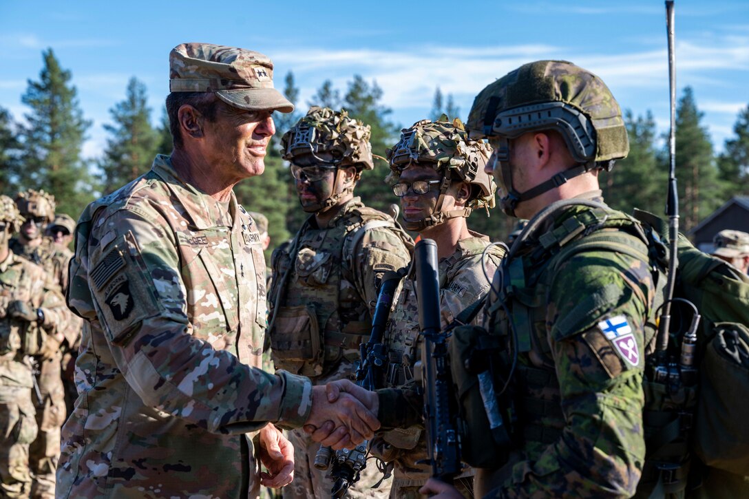 A U.S. and a Finnish soldier shake hands while other soldiers look on.