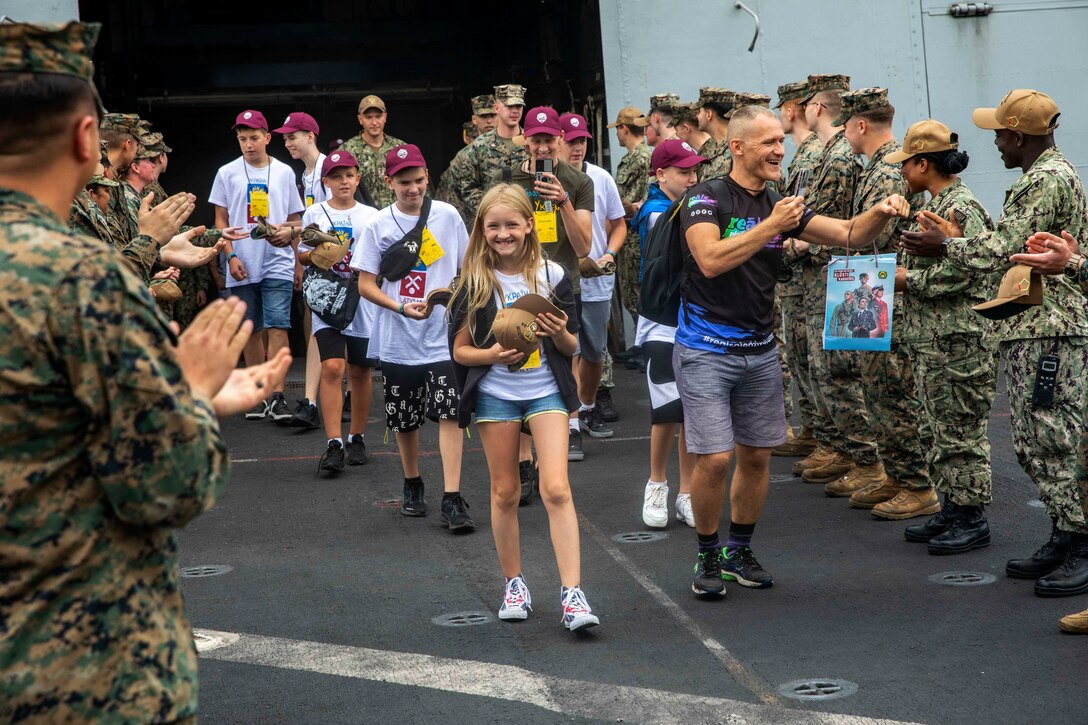 Service members welcome a group of children aboard a ship.