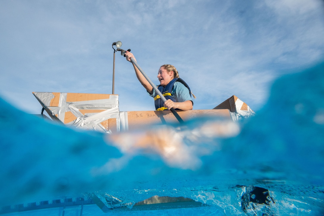 An airman paddles a cardboard boat through the water.