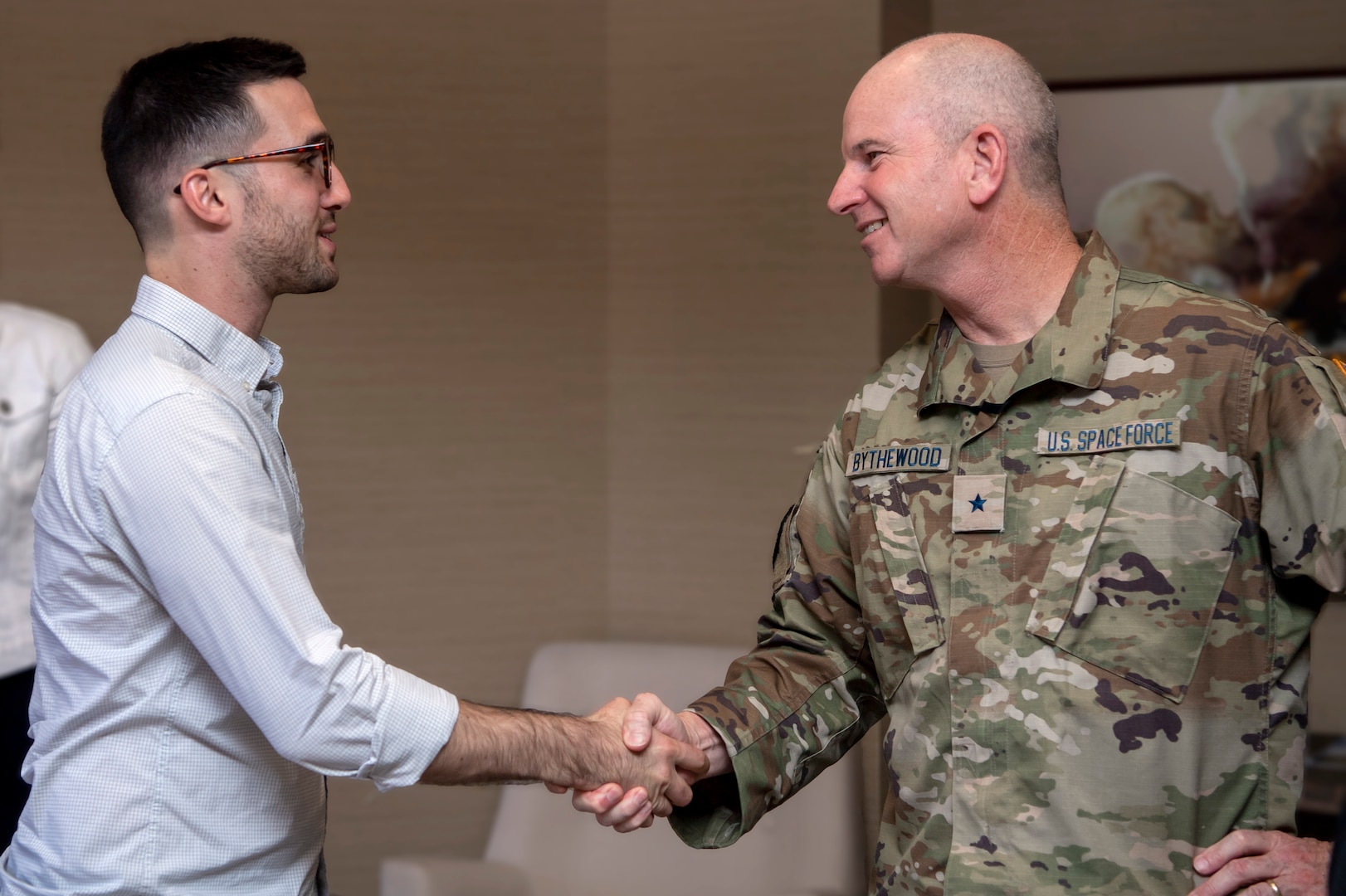 Man in civilian clothes shakes hands with man in military uniform