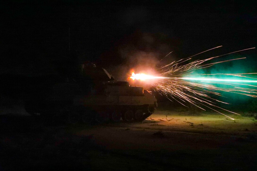 A tank fires at night.