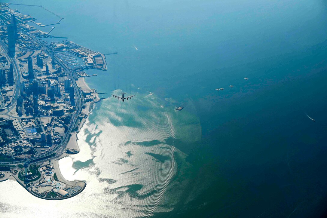 An aircraft flies over water near the coast of a city.