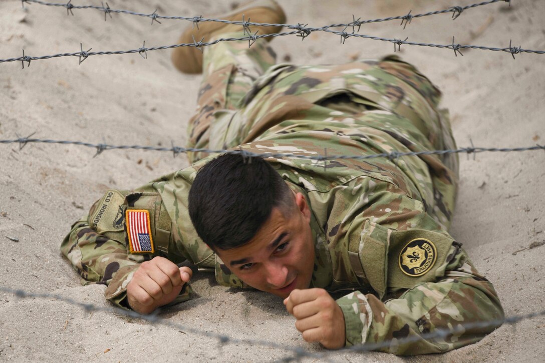 A soldier crawls under a wire obstacle.