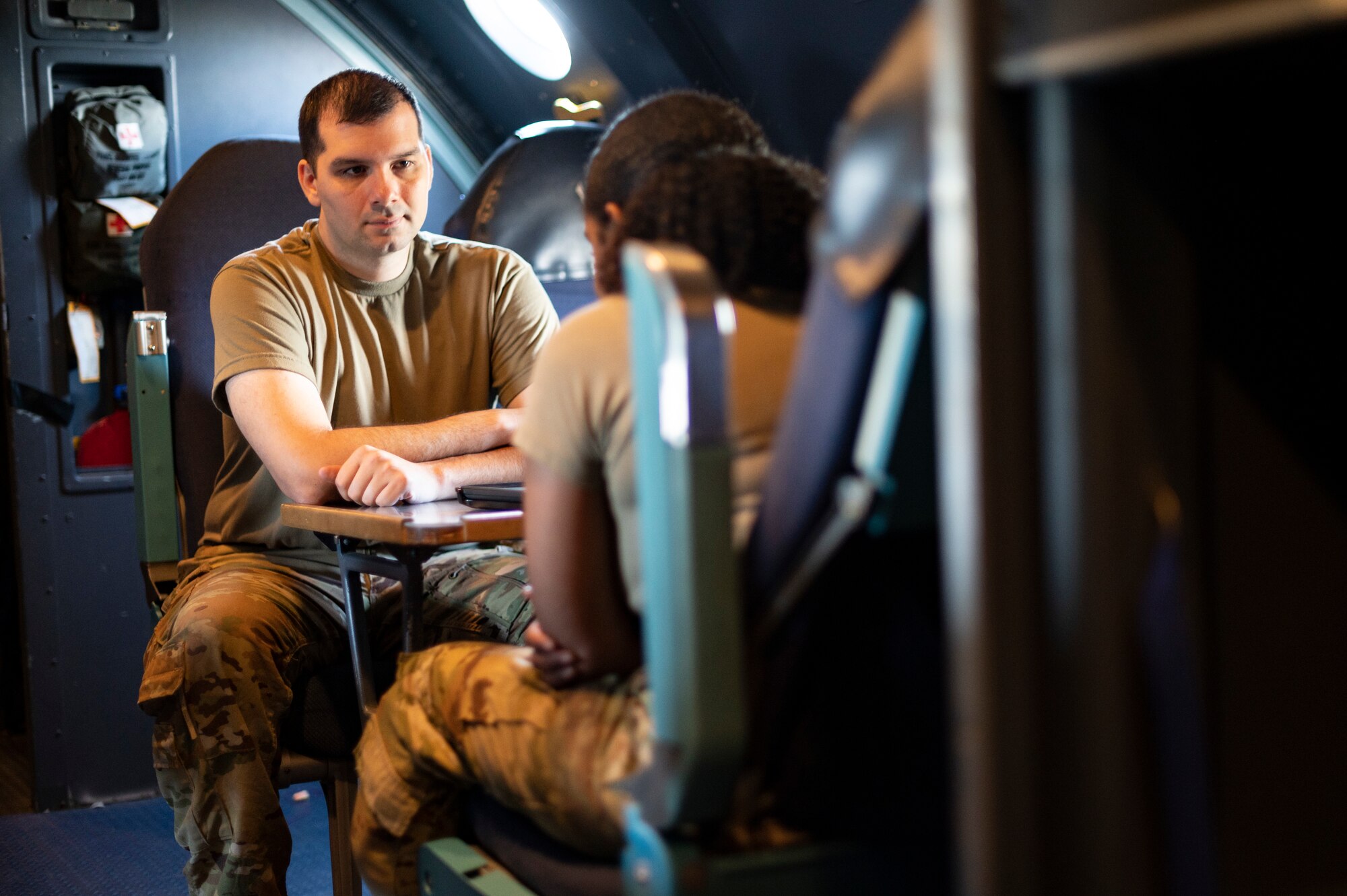 2 Airmen sit at a table on an aircraft.