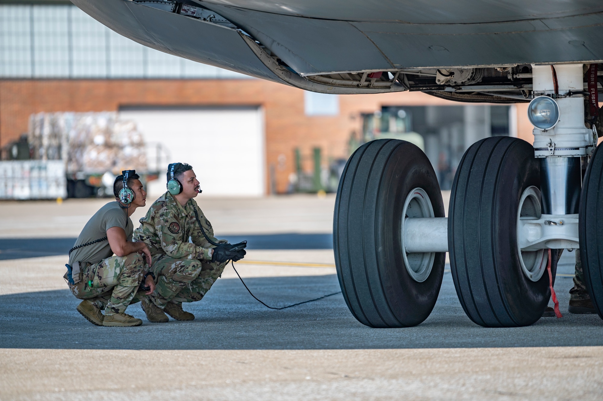 2 Airmen crouch and look at large aircraft wheels.