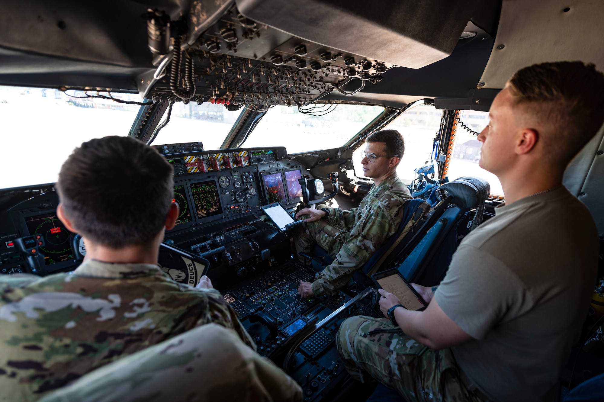 3 Airmen sit in the flight deck of a large aircraft.