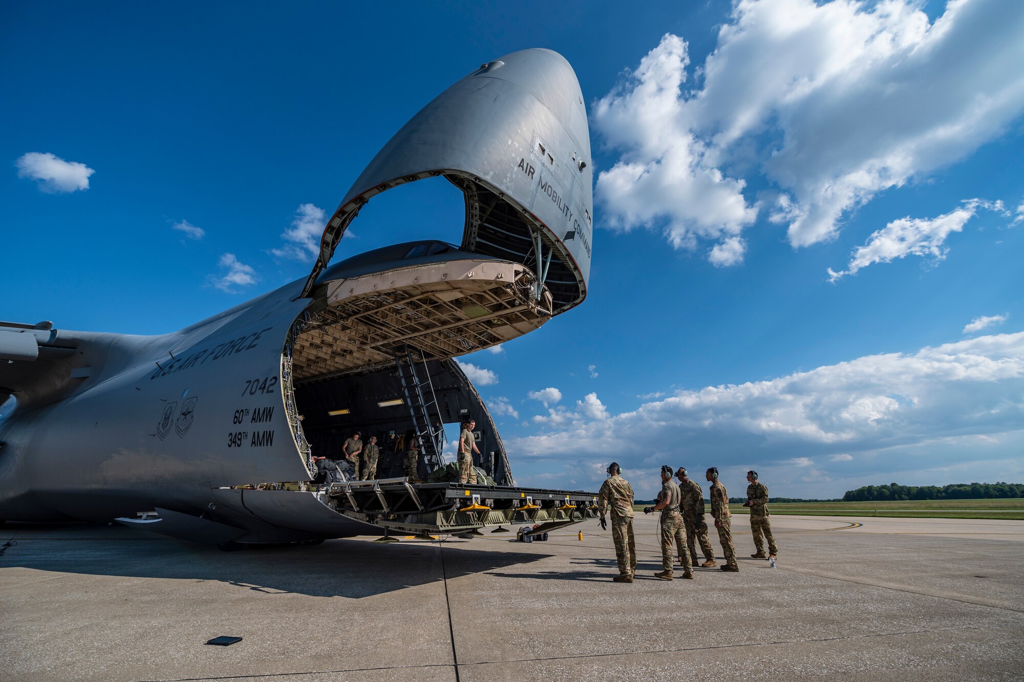 The cargo door to a large aircraft is open as Airmen walk towards the aircraft.
