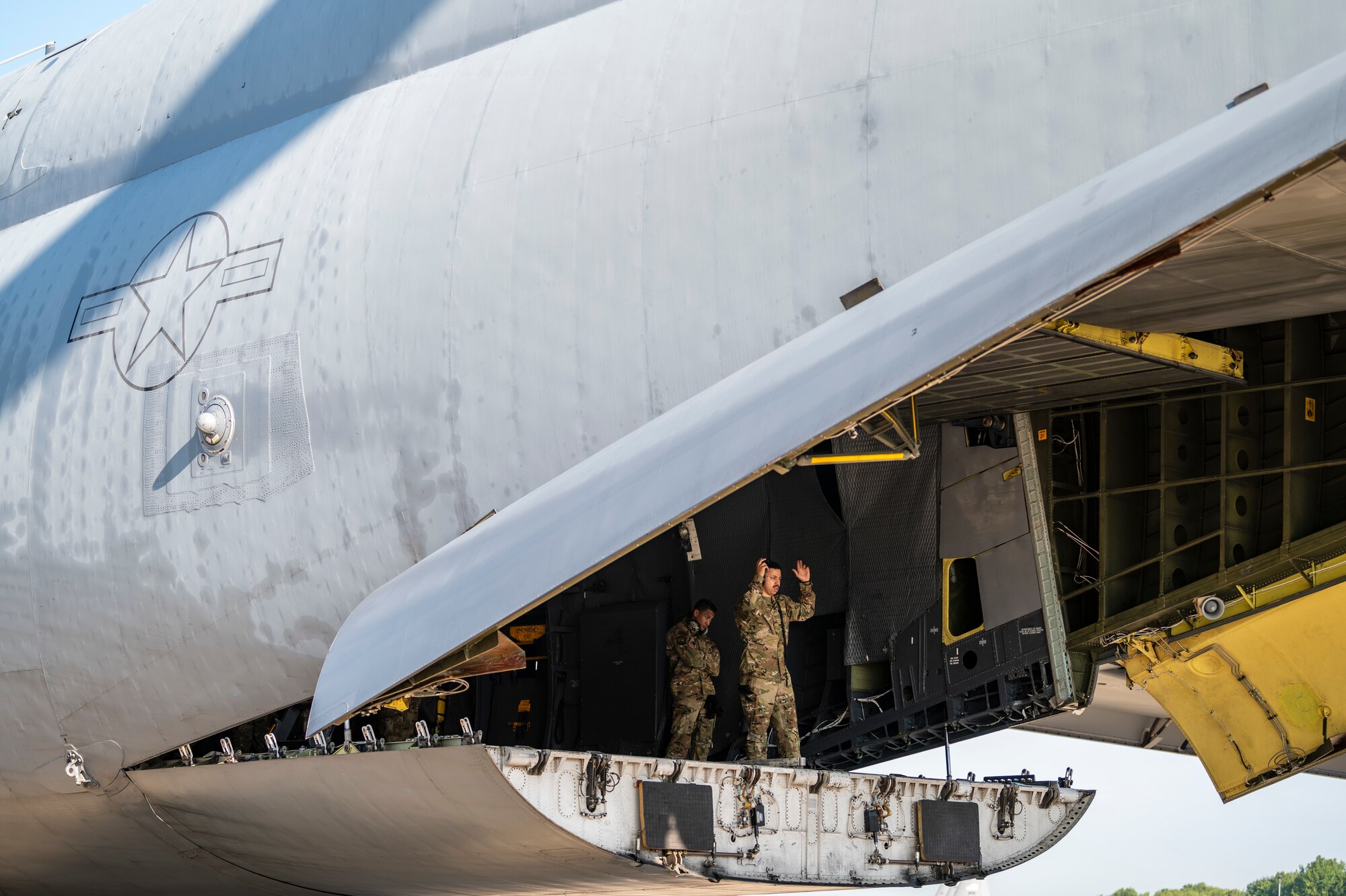 The cargo doors of a large aircraft is open with Airmen inside.