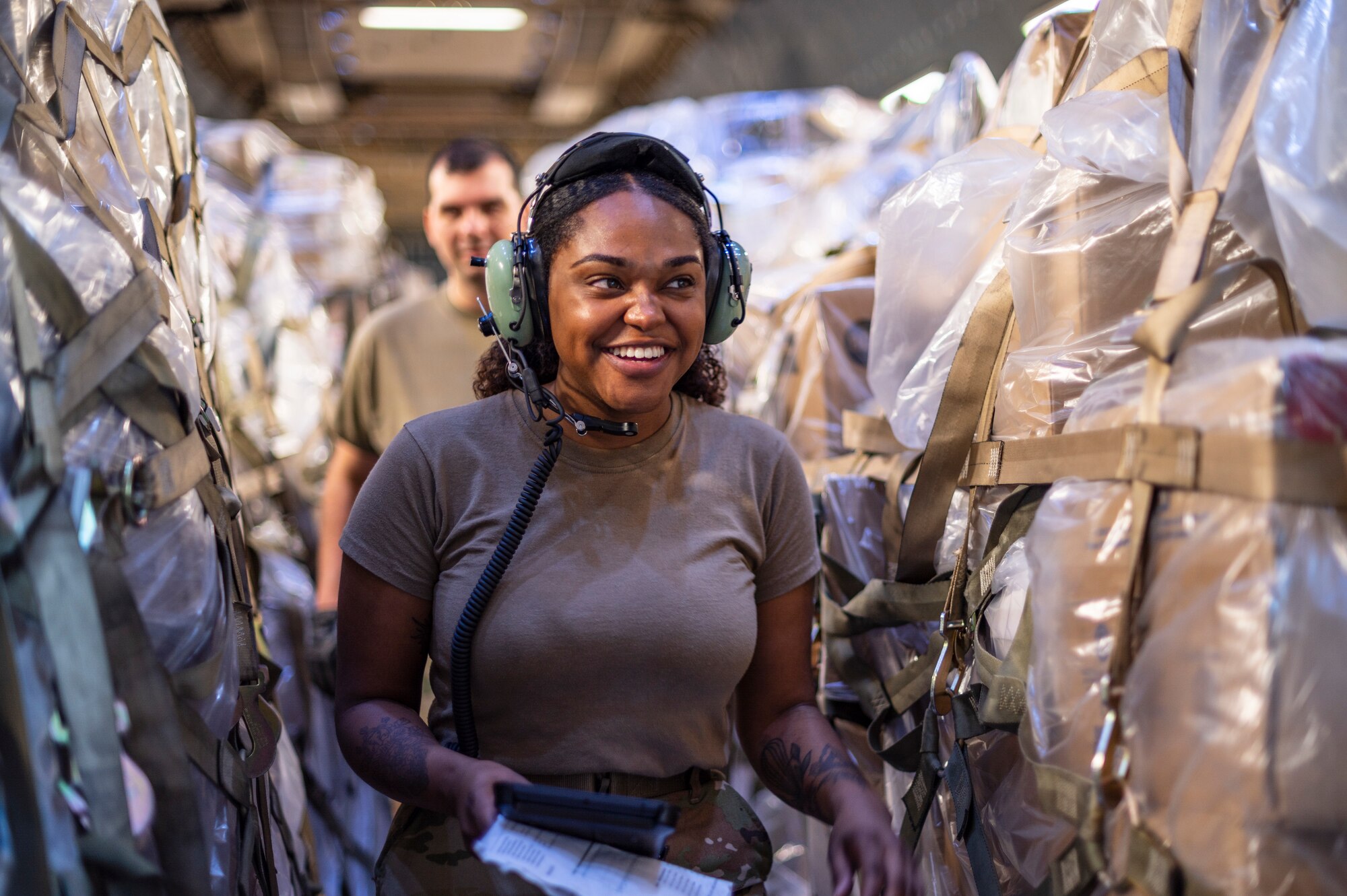 An Airman smiles while walking through pallets of cargo.