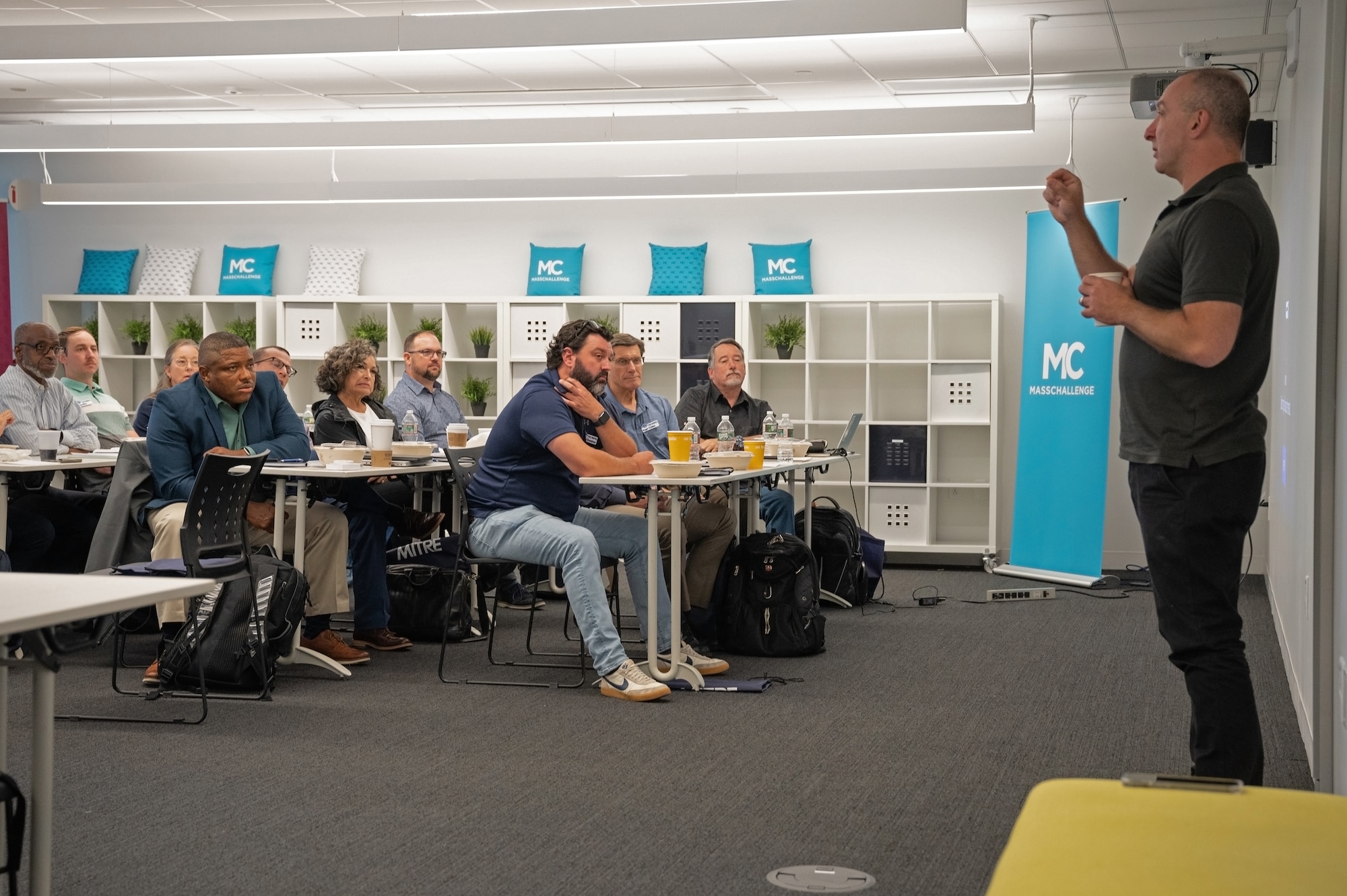 Gene Keselman, right, Massachusetts Institute of Technology Innovation Initiative executive director, speaks to attendees of the Base Camp acquisition innovation pilot program kickoff event at MassChallenge, Boston, Sept. 7.