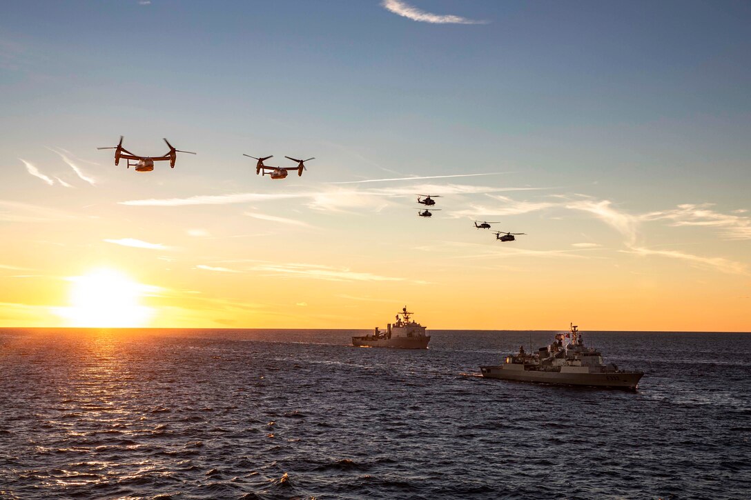 Military aircraft fly over two naval ships at sea.