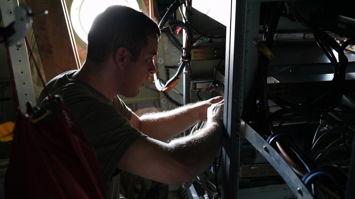 Shows a male Airman reattaching the wiring harness for the new computer on a military aircraft.