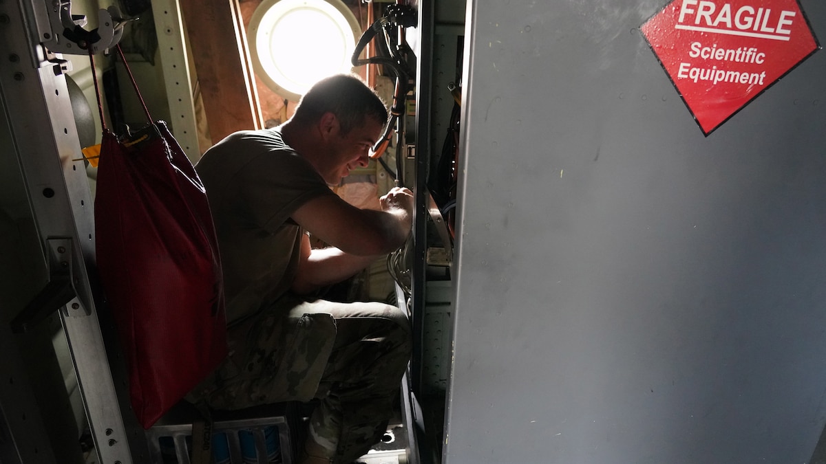 Shows male Airman reattaching cables to the back of computer inside inside of a military aircraft.