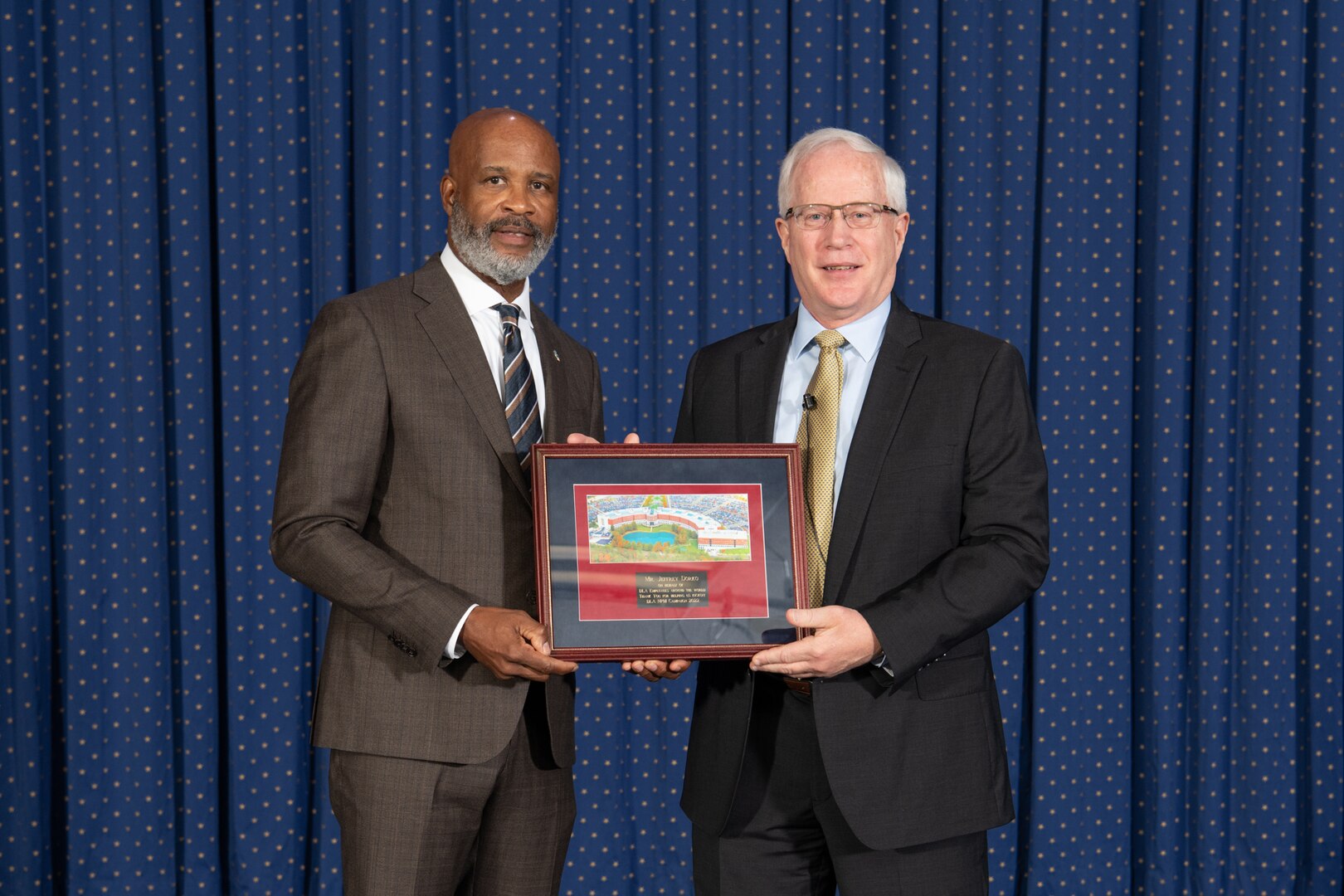 Two men hold a plaque in front of a curtain.