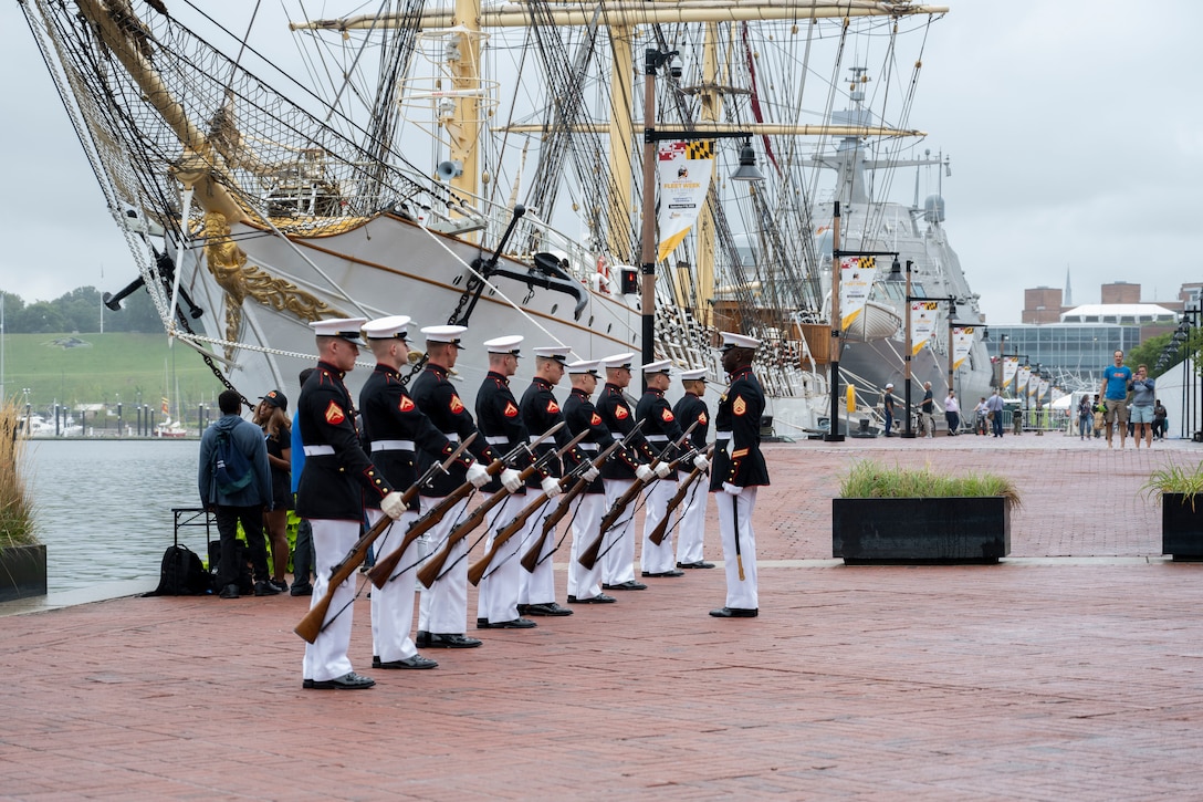 A row of Marines in formal uniforms perform a drill.