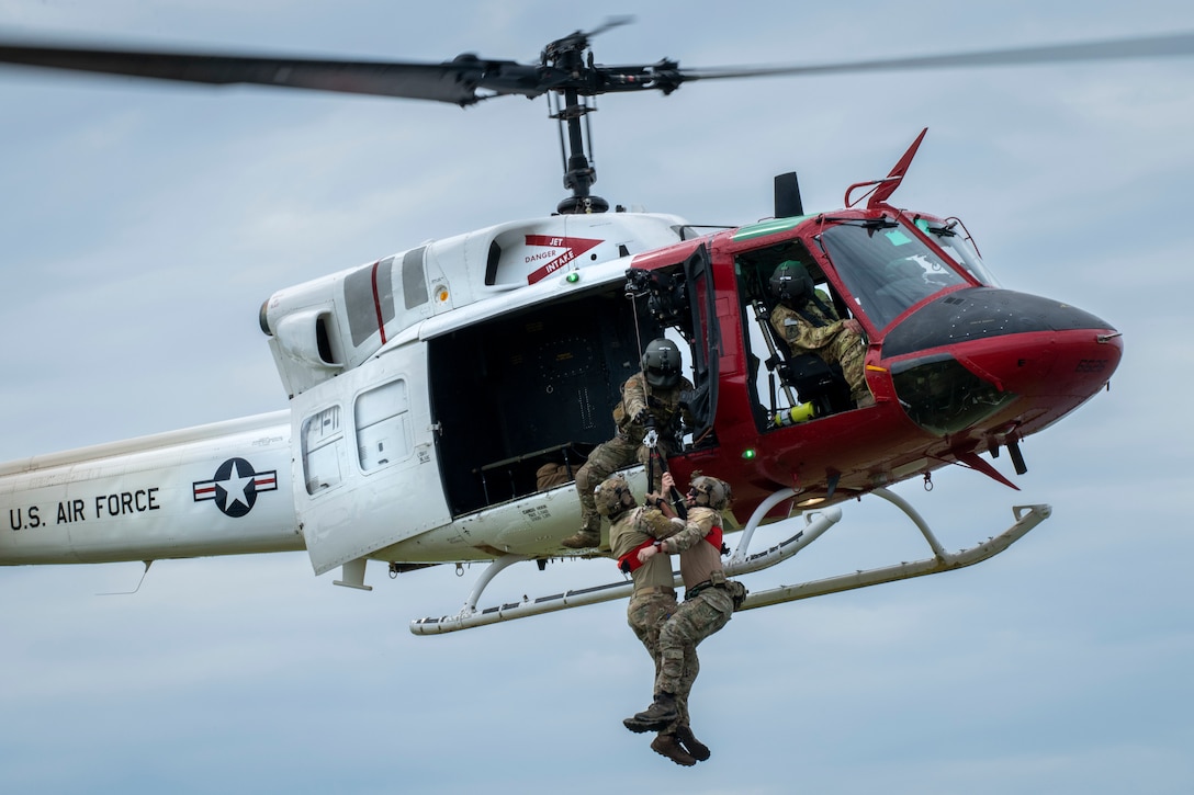 An airman pulls two other airmen into a helicopter.