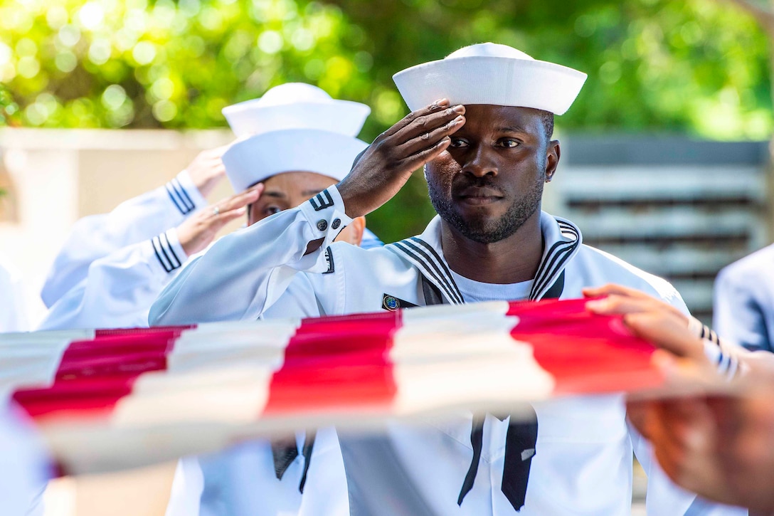 Three sailors salute an American flag held horizontally.