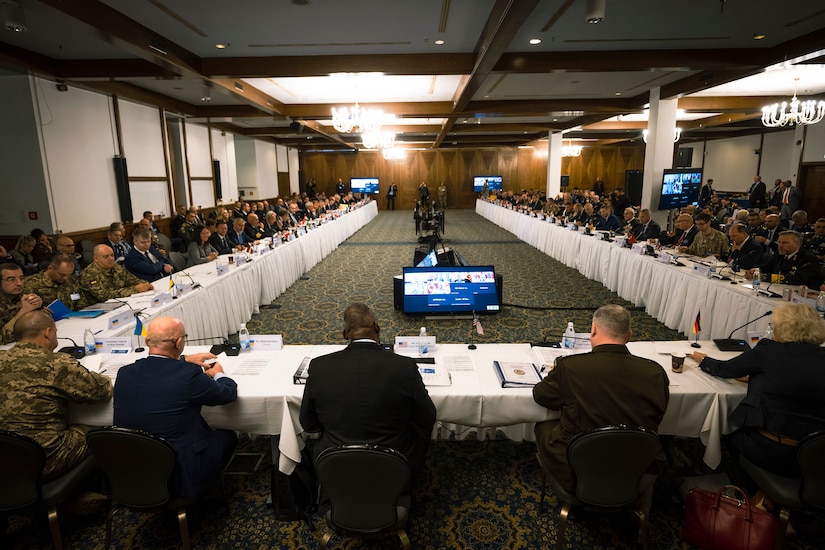 Secretary of Defense Lloyd J. Austin III sits at a long U-shaped table with officials from multiple nations.
