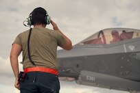 A photo of 1st Lt. Kelsey Flannery, an F-35A Lightning II pilot assigned to the 134th Fighter Squadron of the Vermont Air National Guard's 158th Fighter Wing, is saluted by her crew chief, Staff Sgt. Nathan Tamburello of the 158th Maintenance Group, as she taxis to take off for a training mission from South Burlington Air National Guard Base, Vermont, Sept. 7, 2022. Flannery, who is the Air National Guard's first female F-35 pilot, made her first flight with the 158th after returning from three years of flight training. (U.S. Air National Guard photo by Master Sgt. Ryan Campbell)