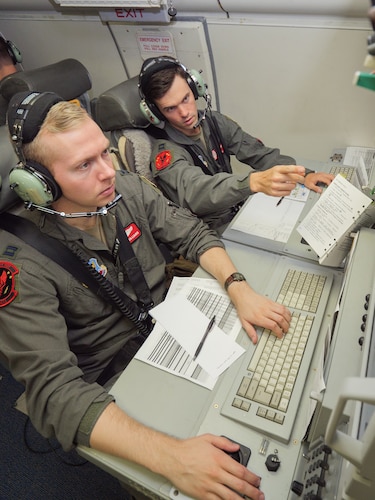 Photo shows two Airmen on aircraft working on computers
