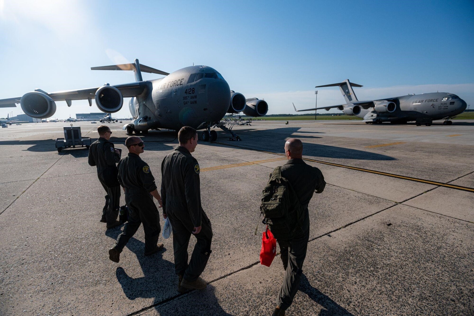 Four men in flight suits walk on a flightline with planes behind them.