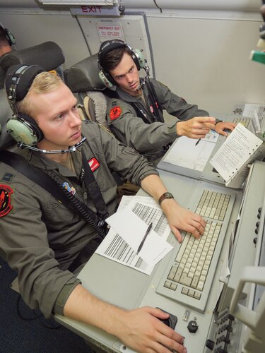 Photo shows two Airmen on aircraft working on computers