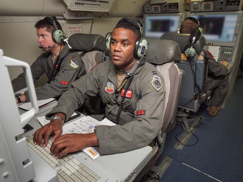 Photo shows Airmen on aircraft working on computers